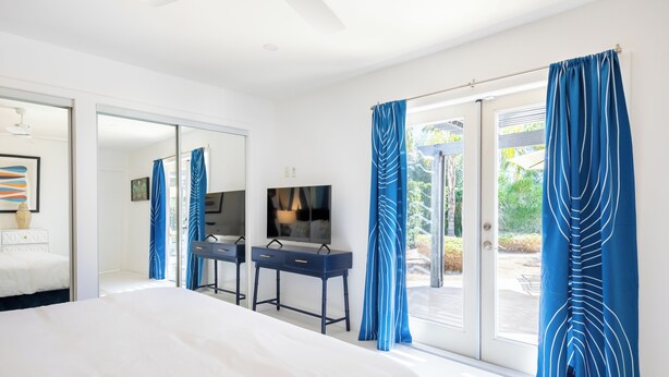 Une chambre d’hôtel moderne dotée d’un grand lit, d’un bureau avec une chaise, d’un téléviseur à écran plat et d’une porte-fenêtre coulissante donnant sur un espace extérieur.