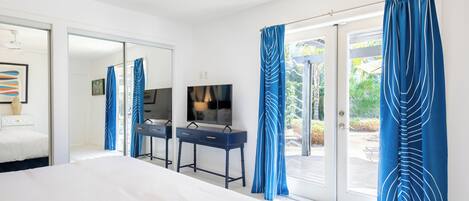 A modern hotel room with a large bed, a desk with a chair, a flat-screen TV, and a sliding glass door leading to an outdoor area.
