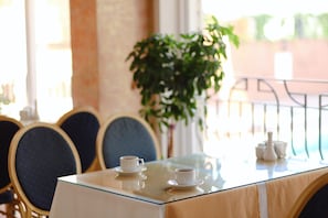 A dining table with two cups of coffee, a glass, and a teapot, surrounded by chairs with dark upholstery.