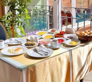 A breakfast table with various dishes and utensils, set on a balcony with a view of a pool and greenery. - Sweet Home Butik Otel (Manavgat)
