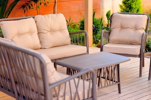 A patio area with a sofa and two chairs, a small table, and a wooden deck.