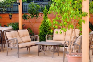 An outdoor seating area with cushioned chairs and a table, surrounded by potted plants and a brick wall. - Sweet Home Butik Otel (Manavgat)