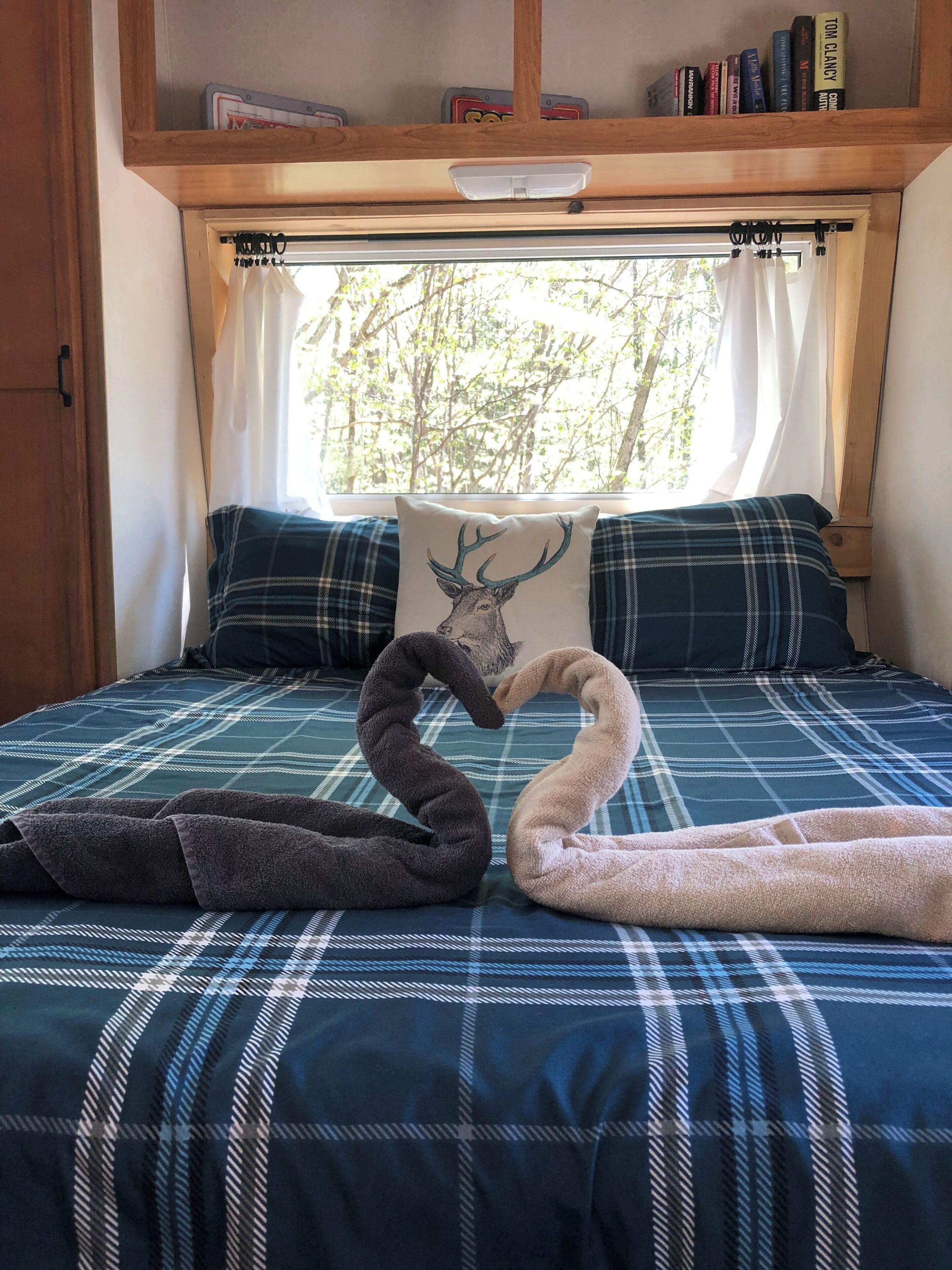 A bed with a plaid bedspread, a pillow with a deer design, and a window with curtains.