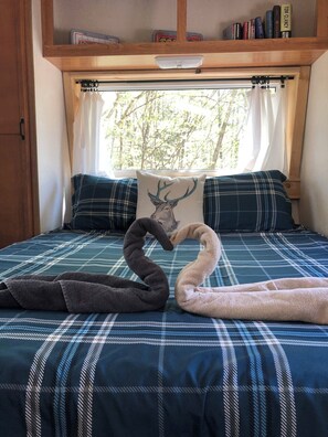 Ein Bett mit einer karierten Tagesdecke, ein Kopfkissen mit einem Hirschmotiv und ein Fenster mit Vorhängen.
