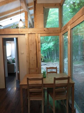 Ein Holzinnenraum mit Esstisch und Stühlen, große Fenster mit Blick auf einen Wald.