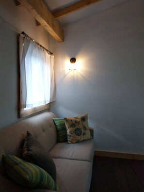 Ein Zimmer mit einer Couch, einem Fenster mit Vorhängen und einer Wandleuchte.