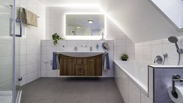 A modern bathroom with a large mirror, a bathtub, a shower area, and a vanity with a sink.
