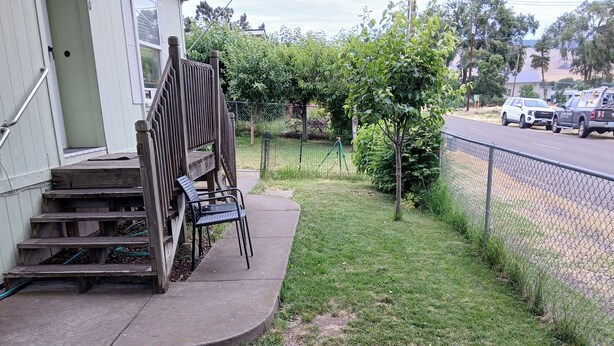 A residential area with a paved driveway, a wooden fence, and a grassy lawn.