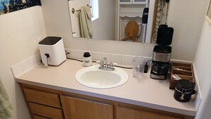 A bathroom with a sink, mirror, towel rack, and a coffee maker.