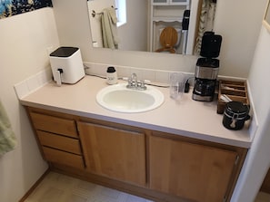 A bathroom with a sink, mirror, towel rack, and a coffee maker.