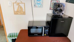 A kitchenette with a microwave, a small refrigerator, and a fan on a table.