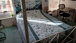 A room with a bed, a desk, a chair, a window with curtains, and a wall with a painting.
