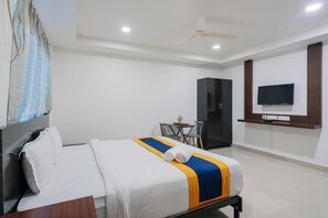 A hotel room with a bed, a desk, a chair, a wardrobe, a television, and a ceiling fan. - Hotel BlueBell Gachibowli By OTABoostup (Hyderabad)