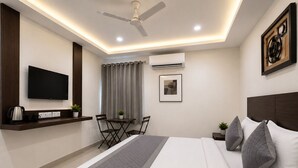 A modern hotel room with a bed, a flat-screen TV, a ceiling fan, an air conditioning unit, a dining table with chairs, and a small side table. - Hotel BlueBell Gachibowli By OTABoostup (Hyderabad)