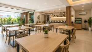 A modern dining area with multiple tables and chairs, a kitchen area with pots and pans, and potted plants. - Hotel BlueBell Gachibowli By OTABoostup (Hyderabad)
