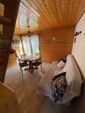 Ein gemütliches Blockhaus-Interieur mit einem Holzesstisch, Stühlen, einer Couch mit Decke und einer Pendelleuchte.
