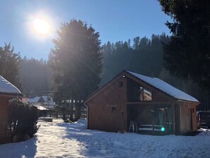 Eine Holzhütte mit geneigtem Dach, umgeben von verschneitem Gelände und Bäumen.