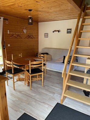 A wooden interior with a dining table, chairs, a sofa, and a wooden staircase. - Myosotis 2 - Cosy chalet Gérardmer | Swimming pool, terrace, pets welcome (Gérardmer)