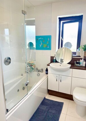 A modern bathroom with a glass shower enclosure, a white sink, and a blue rug. - Cosy Family Home Close to Popular Beaches (Hayle)