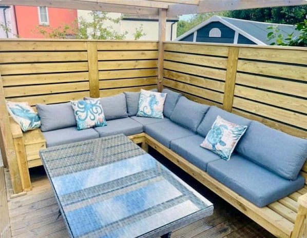 Una terraza de madera con un sofá seccional gris y una mesa de centro de vidrio.