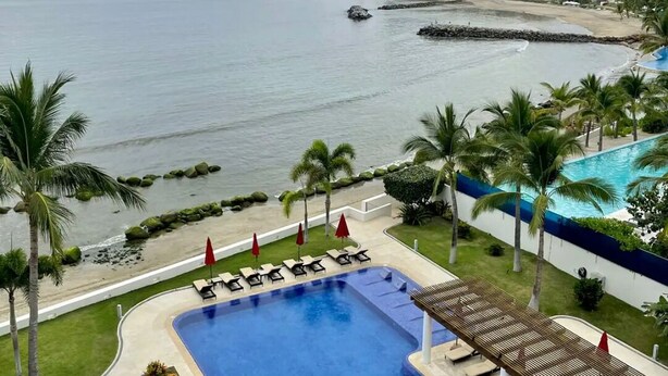 A pool with lounge chairs and umbrellas, a beach, and a view of the ocean. - Exclusive Beachfront Luxury Apartment in La Cruz de Huanacaxtle (Cruz de Huanacaxtle)