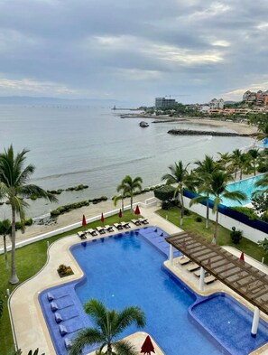 A pool with lounge chairs and umbrellas, a beach, and a view of the ocean. - Exclusive Beachfront Luxury Apartment in La Cruz de Huanacaxtle (Cruz de Huanacaxtle)