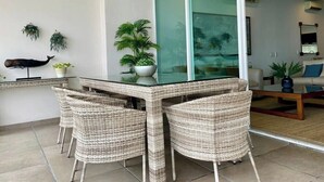 A dining area with wicker furniture, a glass-top table, ceiling fans, and potted plants. - Exclusive Beachfront Luxury Apartment in La Cruz de Huanacaxtle (Cruz de Huanacaxtle)