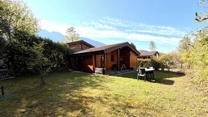 Eine Holzjagdhaushütte mit Terrasse, umgeben von Bäumen und einem Berg im Hintergrund.