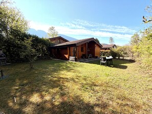 Eine Holzjagdhaushütte mit Terrasse, umgeben von Bäumen und einem Berg im Hintergrund.