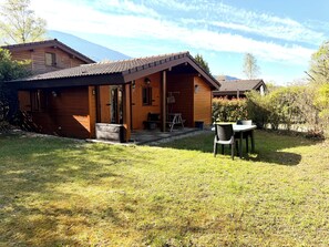 A wooden cabin with a covered porch, a table and chairs outside, and a mountain backdrop. - Chalet ideally located on the shores of Lake Annecy (Doussard)