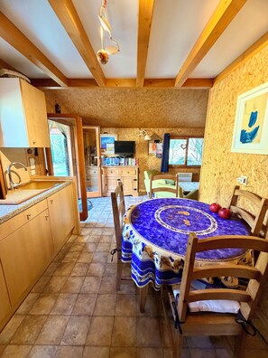 Eine Küche mit Holzbalken, einem Esstisch mit blauer Tischdecke und einem Fernseher im Hintergrund.