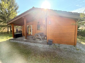 A wooden cabin with a covered porch, a grill, and a picnic table. - Chalet ideally located on the shores of Lake Annecy (Doussard)