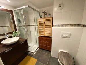 A bathroom with a glass-enclosed shower, a wooden cabinet, a white sink, and a toilet. - "Le Tina" 2-Bedroom Duplex Near the Harbor—Wi-Fi, Air Conditioning, Parking (La Ciotat)
