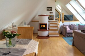 A cozy loft-style room with a fireplace, a sofa, a television, and a wooden staircase. - The vacation apartment in beautiful natural surroundings Relax, unwind and feel good (Hinterzarten)