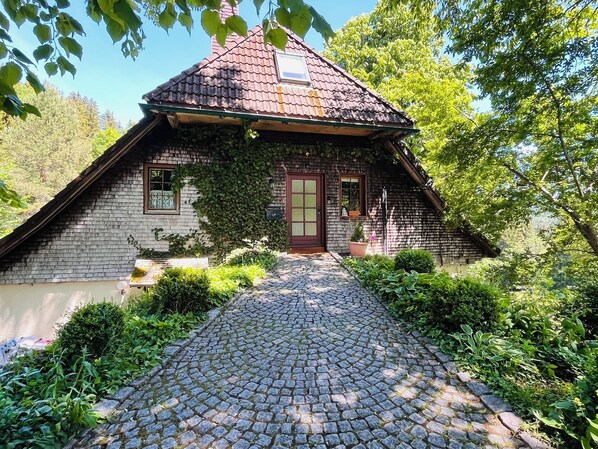 A rustic house with a tiled roof, a wooden door, and a cobblestone pathway leading to the entrance. - The vacation apartment in beautiful natural surroundings Relax, unwind and feel good (Hinterzarten)