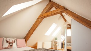 A bedroom with a sloped ceiling, a bed with patterned bedding, a wooden headboard, and a small plant on a white dresser. - The vacation apartment in beautiful natural surroundings Relax, unwind and feel good (Hinterzarten)