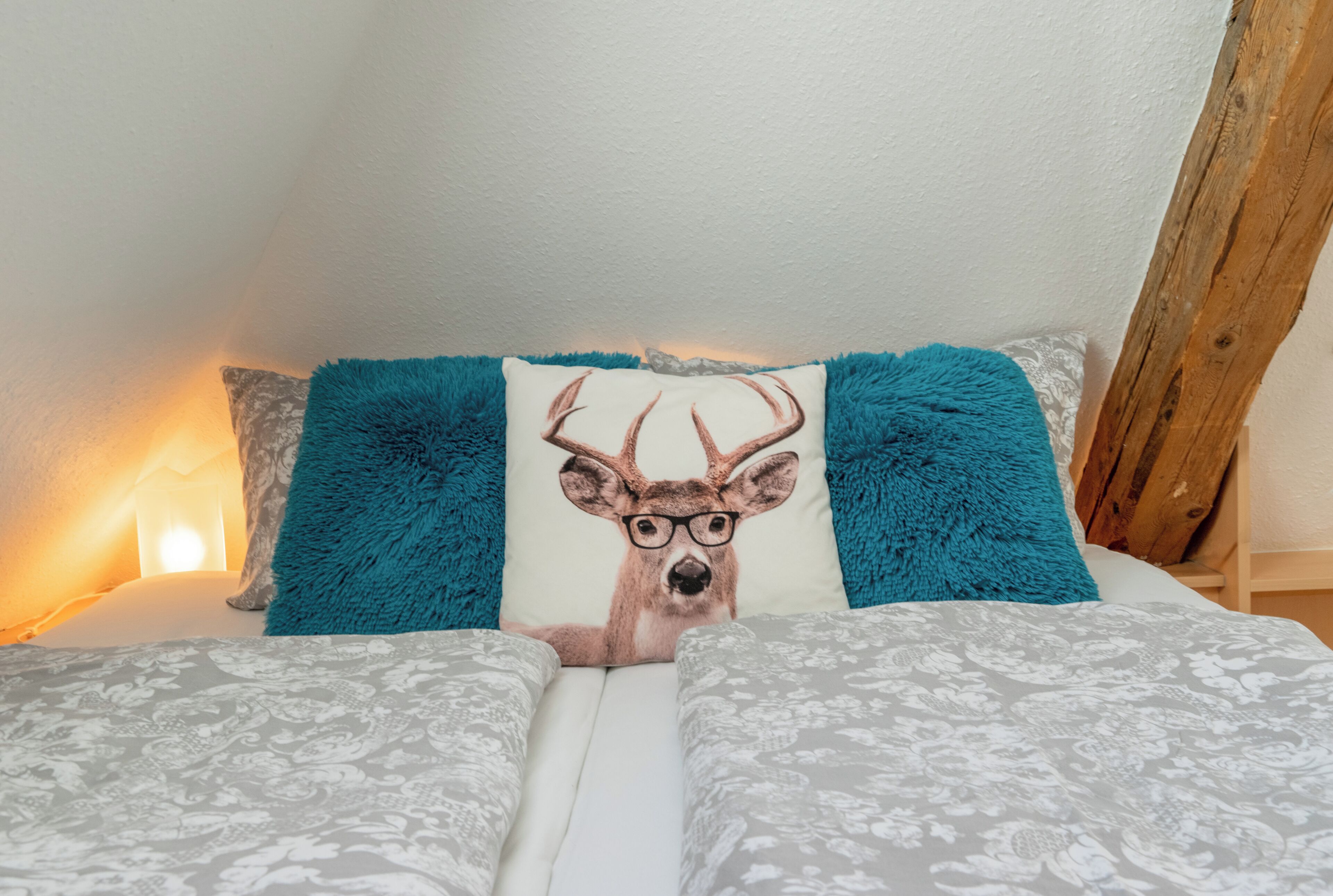 A bed with patterned bedding, a teal pillow with a deer design, and a wooden headboard.