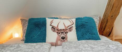 A bed with patterned bedding, a teal pillow with a deer design, and a wooden headboard.