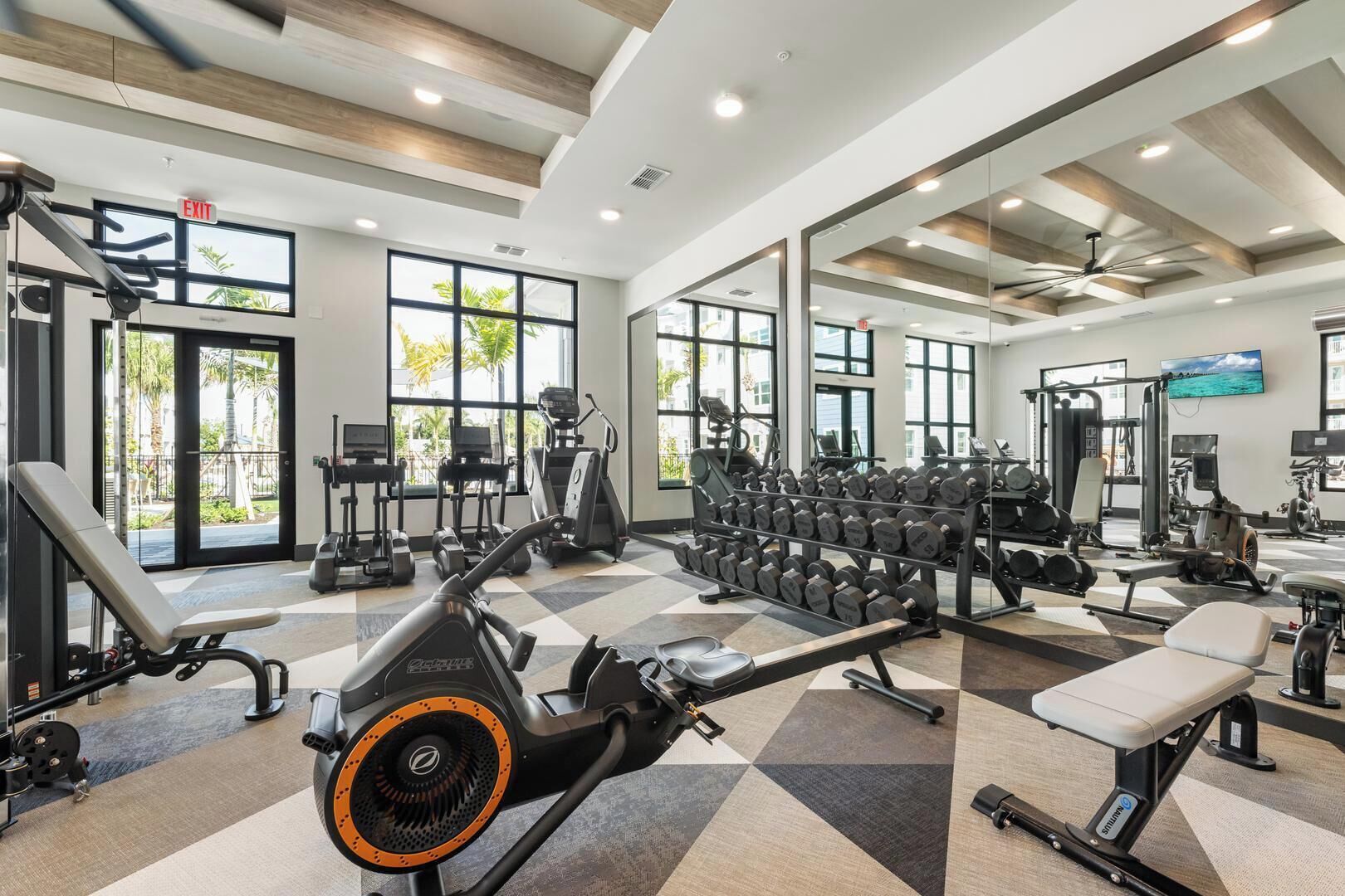 Et fitnesscenter med løbebånd, styrketræningsudstyr og store vinduer.