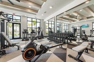 Un gimnasio con máquinas de cardio, equipo de levantamiento de pesas y amplios ventanales.