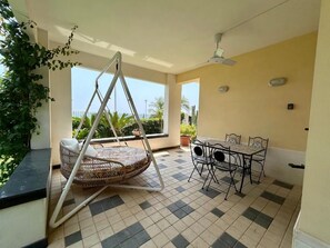 Ein Zimmer mit Schaukelstuhl, Esstisch mit Stühlen, Deckenventilator und Blick ins Freie.
