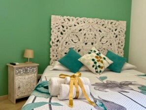 Ein ordentlich bezogenes Bett mit einem dekorativen Kopfteil, einem aufgerollten Handtuch und einem Nachttisch mit Lampe.