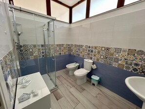 Ein Badezimmer mit Dusche, zwei Toiletten, einem Waschbecken und einer gefliesten Rückwand.
