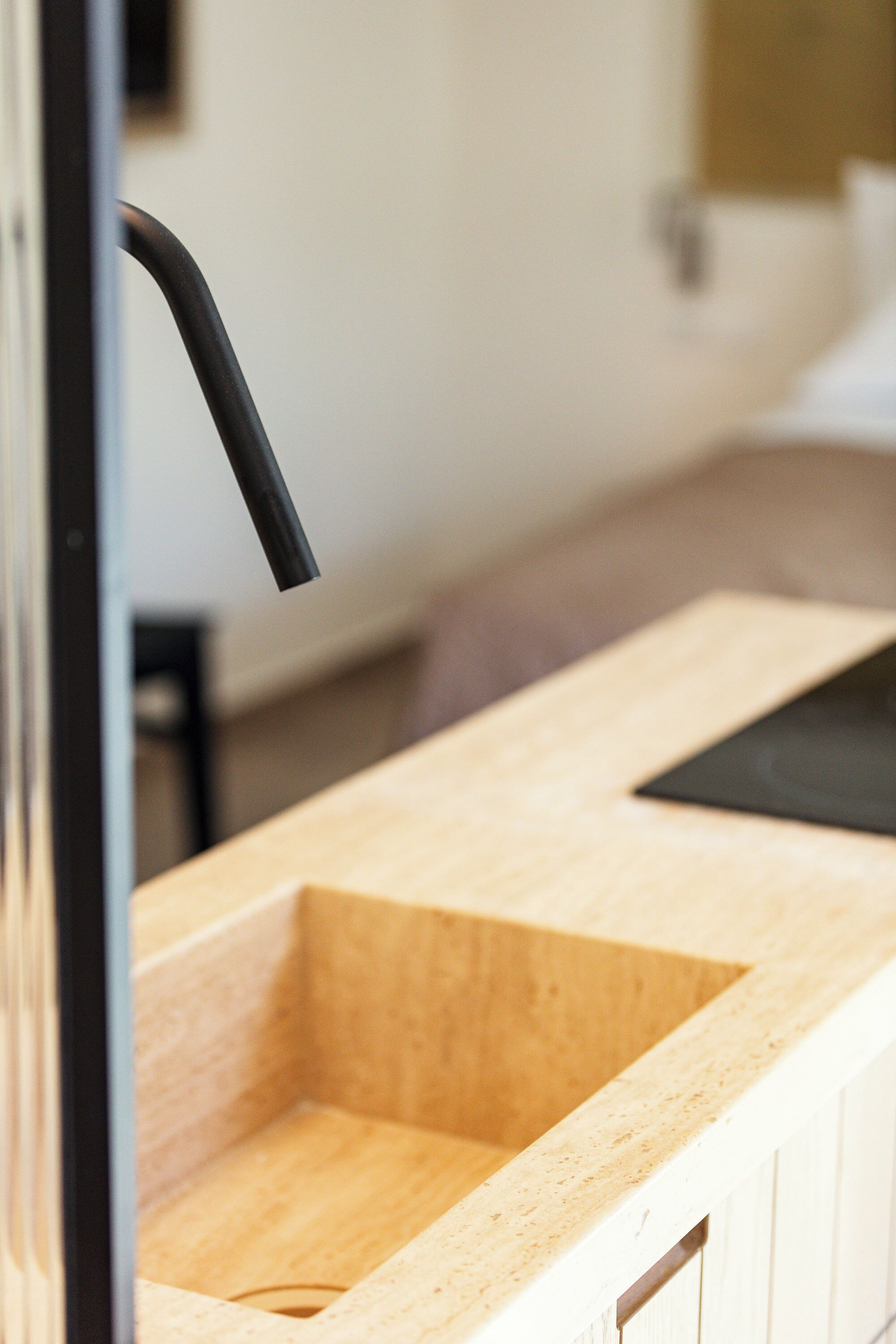 Eine Holzausziehtafel mit einem schwarzen Wasserhahn, einem Spülbecken und einer weißen Wand im Hintergrund.