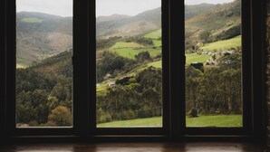 A view through a window with a rural landscape, including hills, fields, and scattered buildings. - Luxury house in front of the valley, 20 minutes from Las Catedrales beach. (San Tirso de Abres)