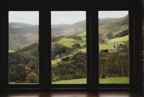 A view through a window with a rural landscape, including hills, fields, and scattered buildings.