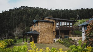 A stone house with a balcony, surrounded by greenery and a forested hill. - Luxury house in front of the valley, 20 minutes from Las Catedrales beach. (San Tirso de Abres)