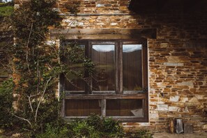A rustic stone building with a large window and wooden shutters.