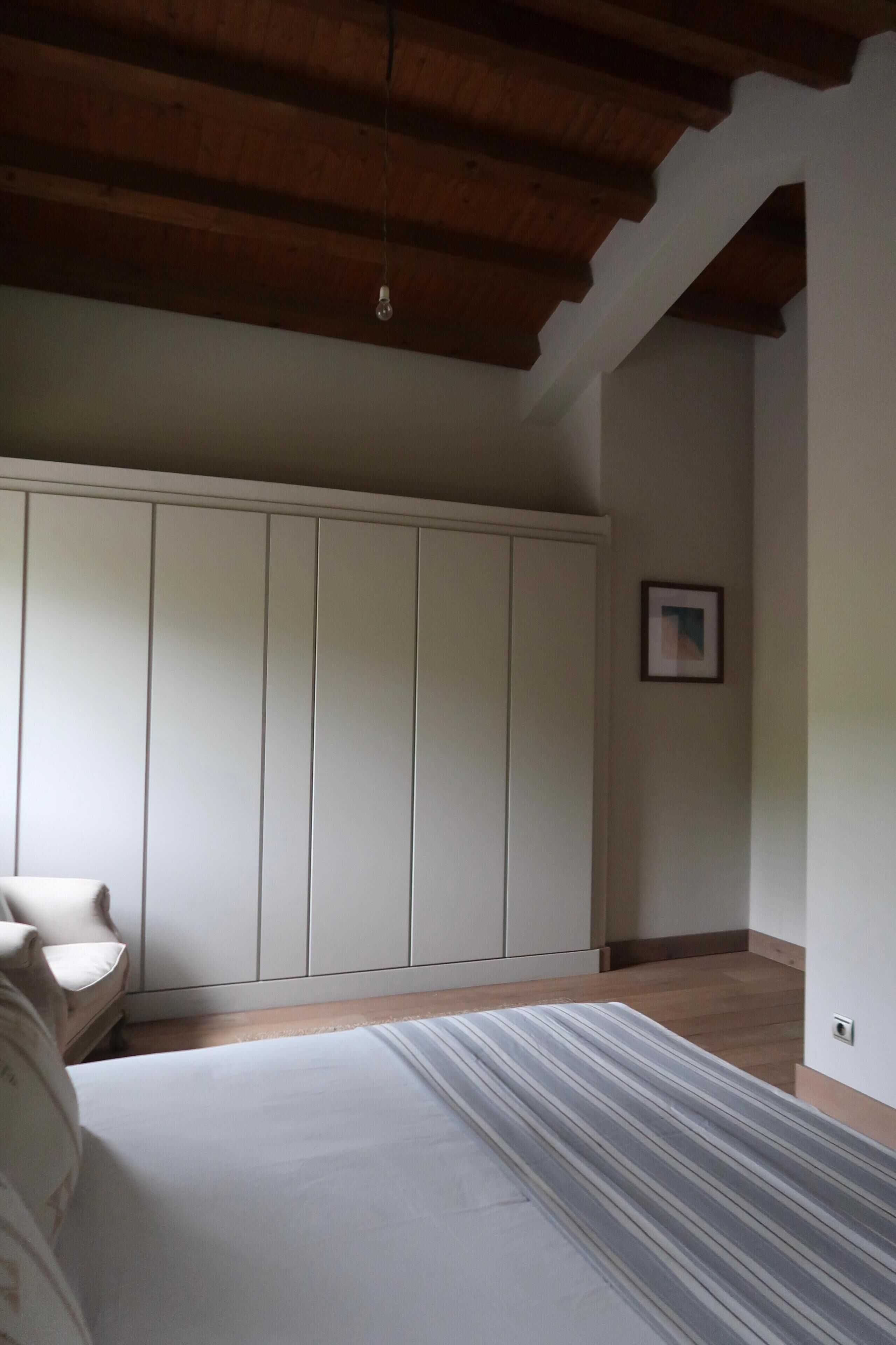 A room with a bed, a wardrobe, a framed picture on the wall, and a wooden ceiling.