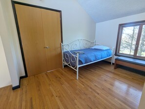 A bedroom with a wooden floor, a metal bed frame, a window with a view, and a door. - Quiet Poconos Chalet with Loft Lounge (ALBRIGHTSVLLE)